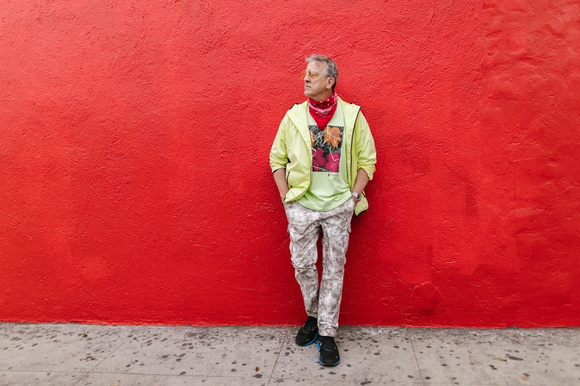a man in a stylish outfit leaning on a red wall