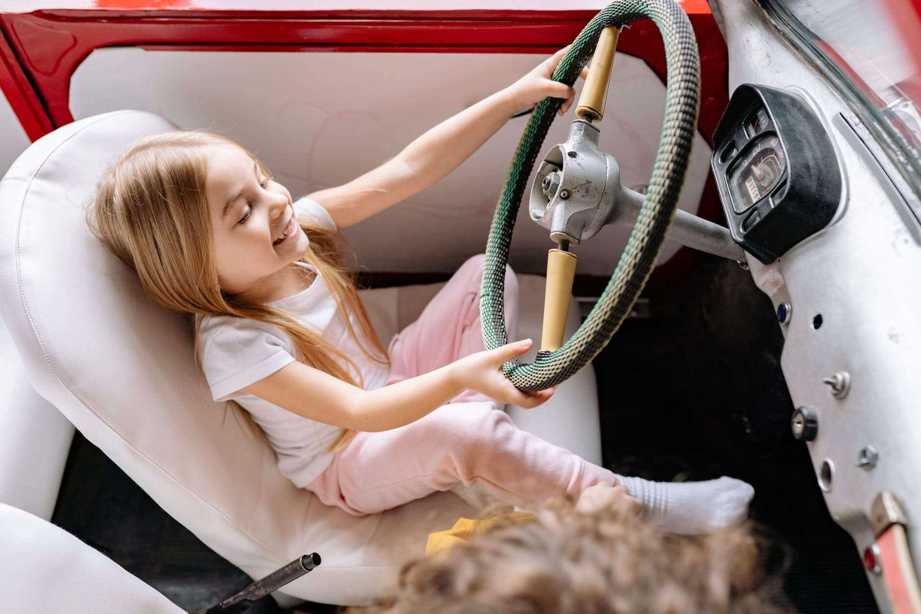 a young girl sitting on the car while playing on steering wheel
