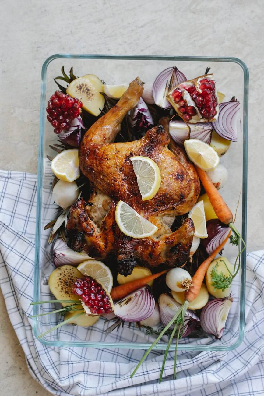 grilled whole chicken with vegetables and fruits in glass bowl